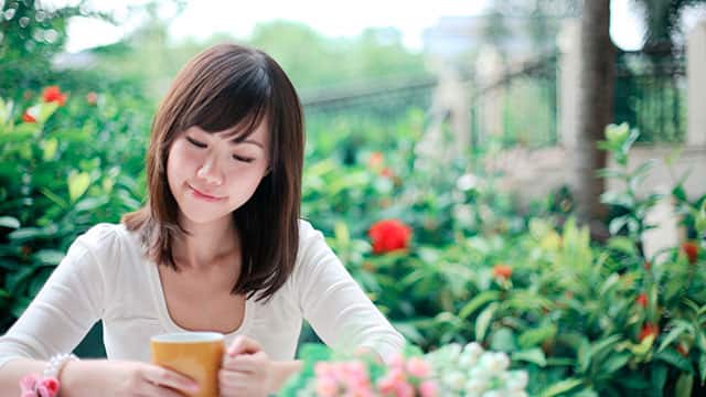A girl smiling in a garden, holding a cup.